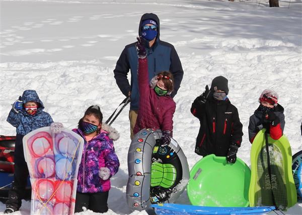 Five students posing in the snow with their sleds in front of their teacher.